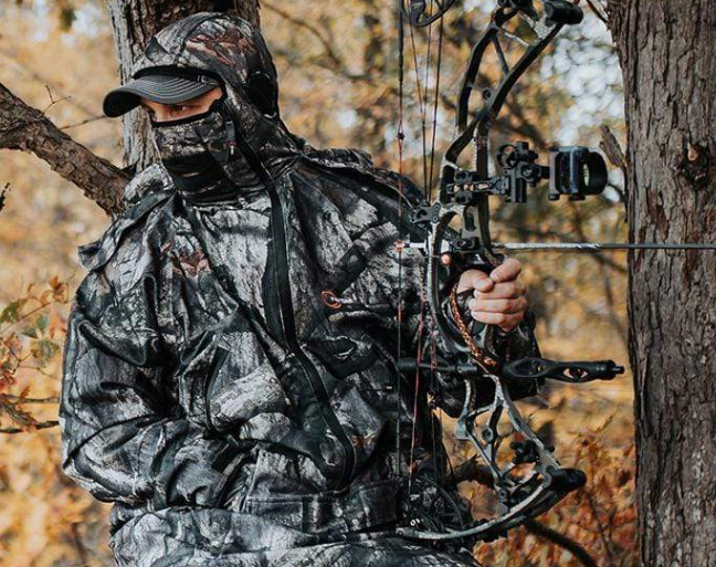 IWOM Hunting suit with mossy oak treestand | Bow hunter in treestand with bow in hand ready to draw. Hunt in comfort this hunting season. 